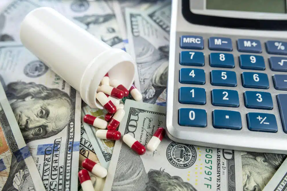 Prescription bottle and pills laying over cash with a calculator next to it.