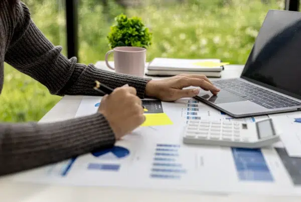 Person reviewing financial charts and calculations on a laptop with paperwork and calculator, illustrating planning for Maximum Broker Commissions 2027.